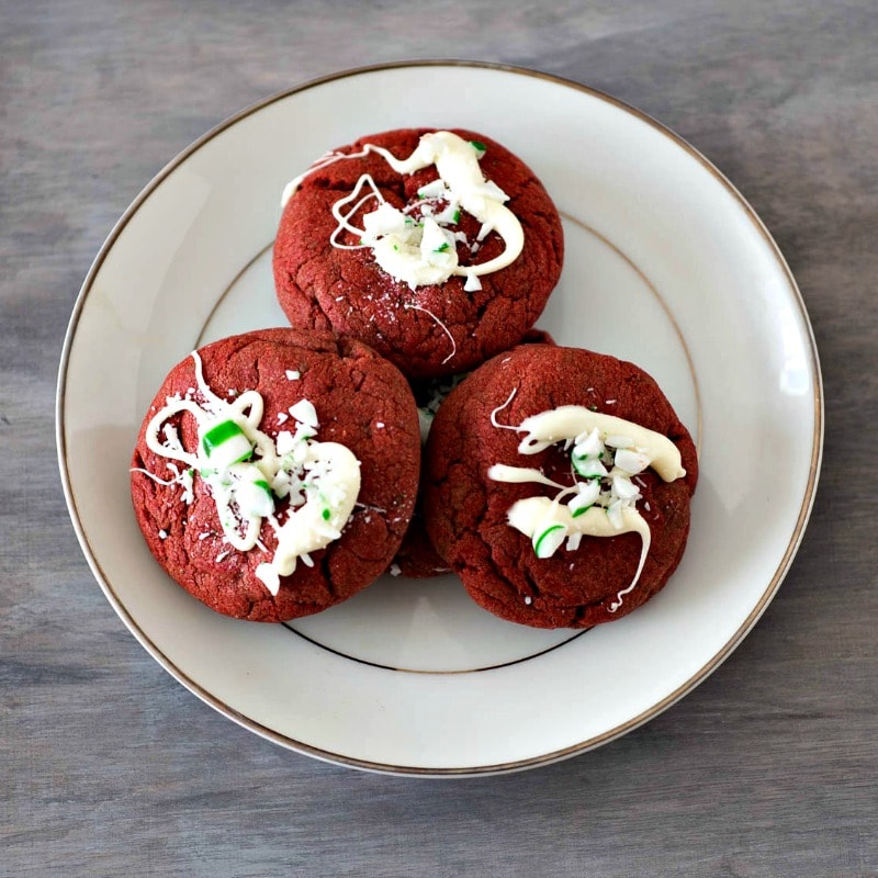Make these Holiday Red Velvet Cookies - they are drizzled with white chocolate and sprinkled with peppermint candy! Easy to make using a cake mix as a base