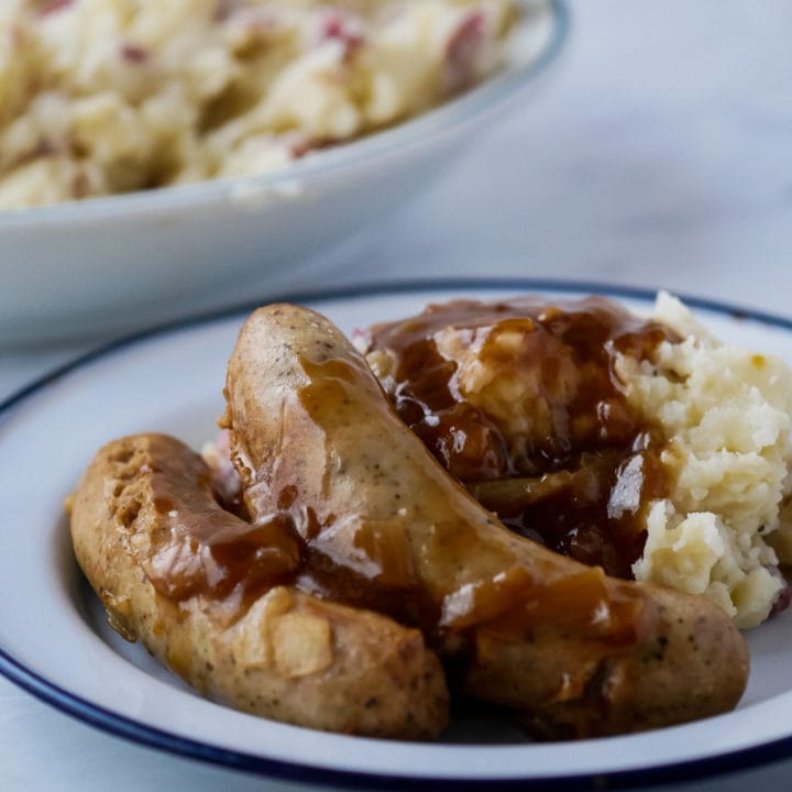 bangers and mash on a plate with mashed potatoes in background