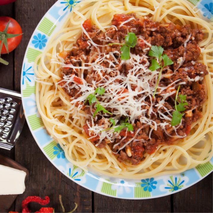 spaghetti topped with bolognese sauce on a blue and white plate