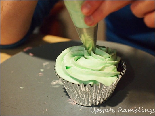 A person is decorating a cupcake with green frosting.