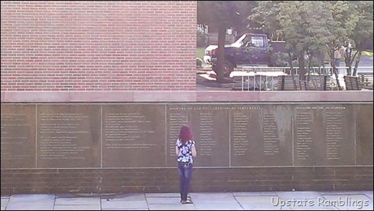 A woman standing in front of a wall with a memorial plaque.