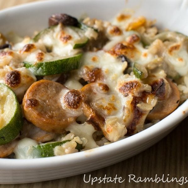 Sliced sausage and zucchini covered in cheese in a casserole dish.