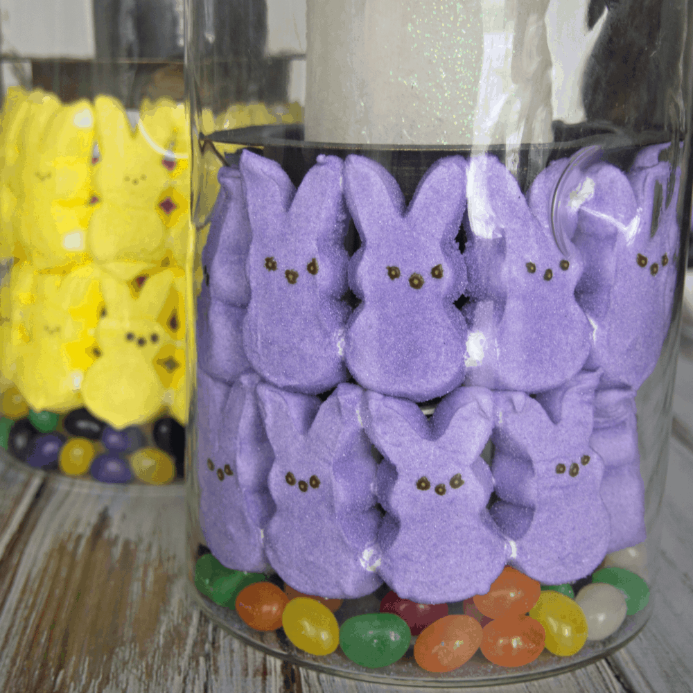 Peeps in glass candle holders on a table.