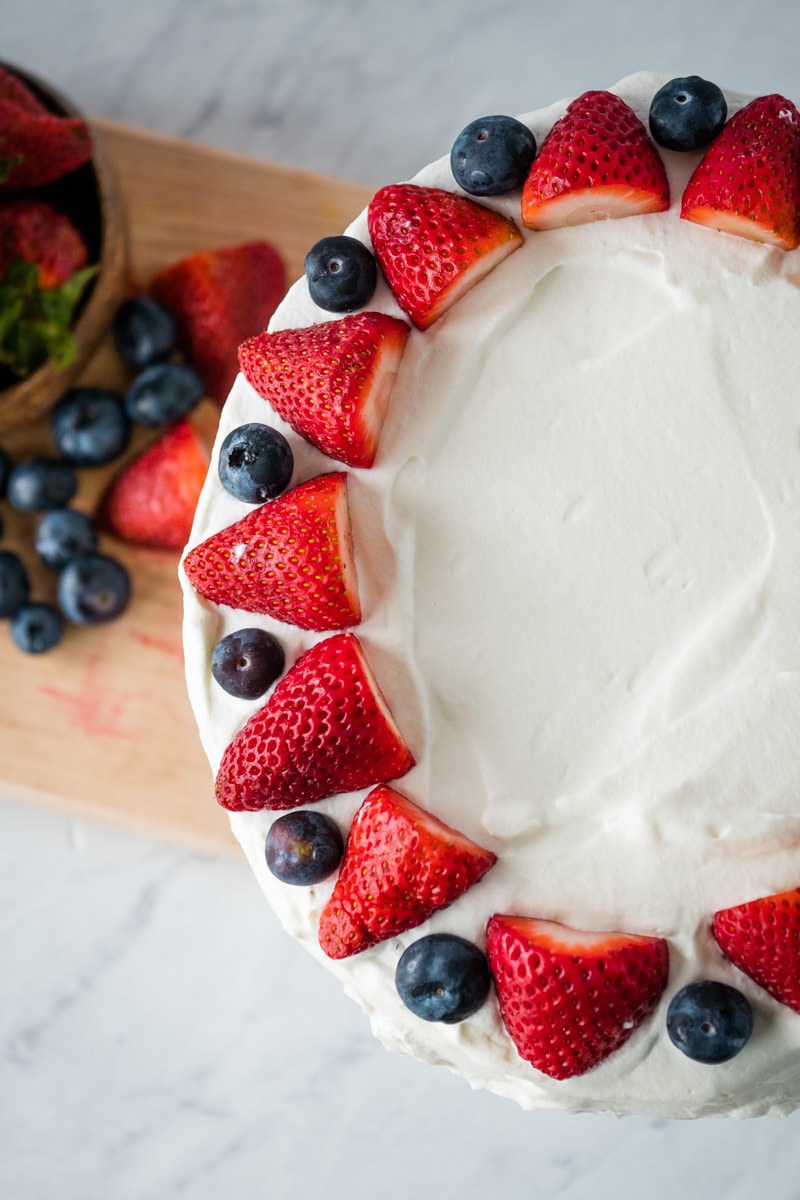 Make this traditional Norwegian Dessert - Bløtkake - a delicious sponge layer cake filled with pudding & peaches & cream, topped with whipped cream, blueberries and strawberries - Norwegian Cream Cake #norwegian #cake #dessert 