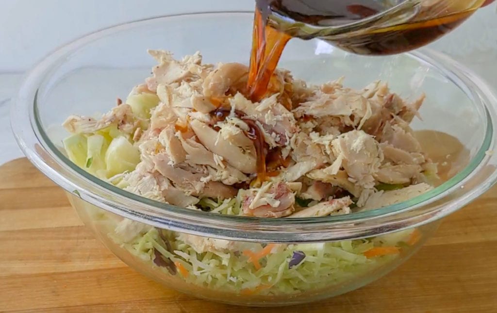 pouring dressing over chicken salad in a bowl.