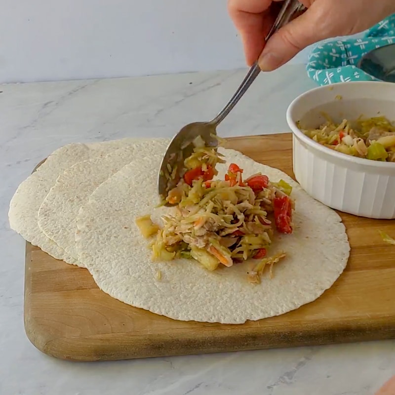 spooning chicken salad onto a tortilla for rolling up into a wrap.