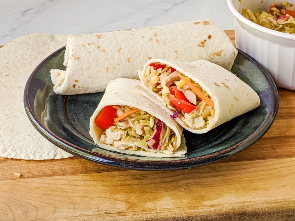 two chicken salad wraps on a plate with one cut in half to show the filling inside