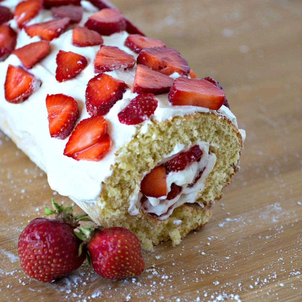A strawberry roll cake with cream and strawberries on a cutting board.