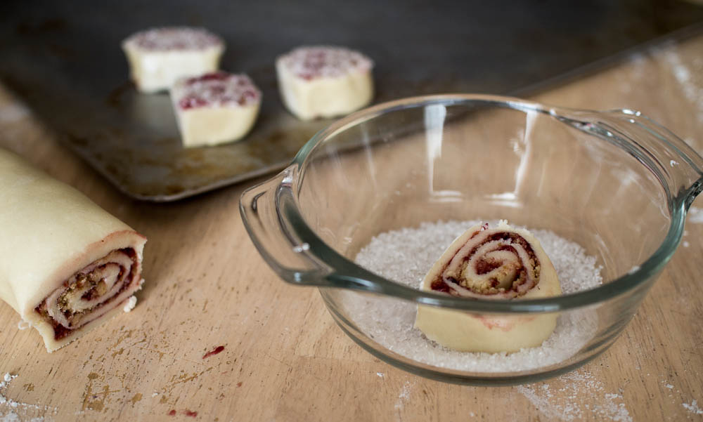 A bowl of cranberry roll ups next to a bowl of sugar and raspberry pinwheel cookies.
