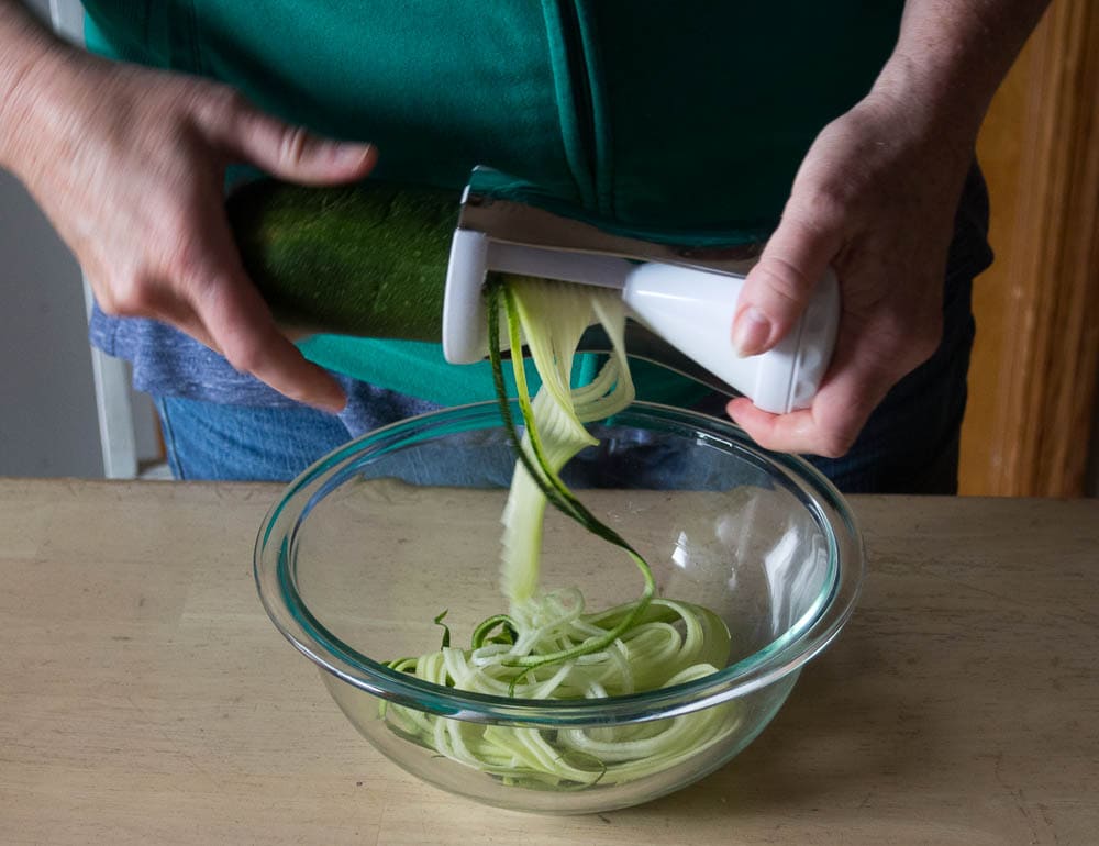 A person slicing zucchini into a bowl.