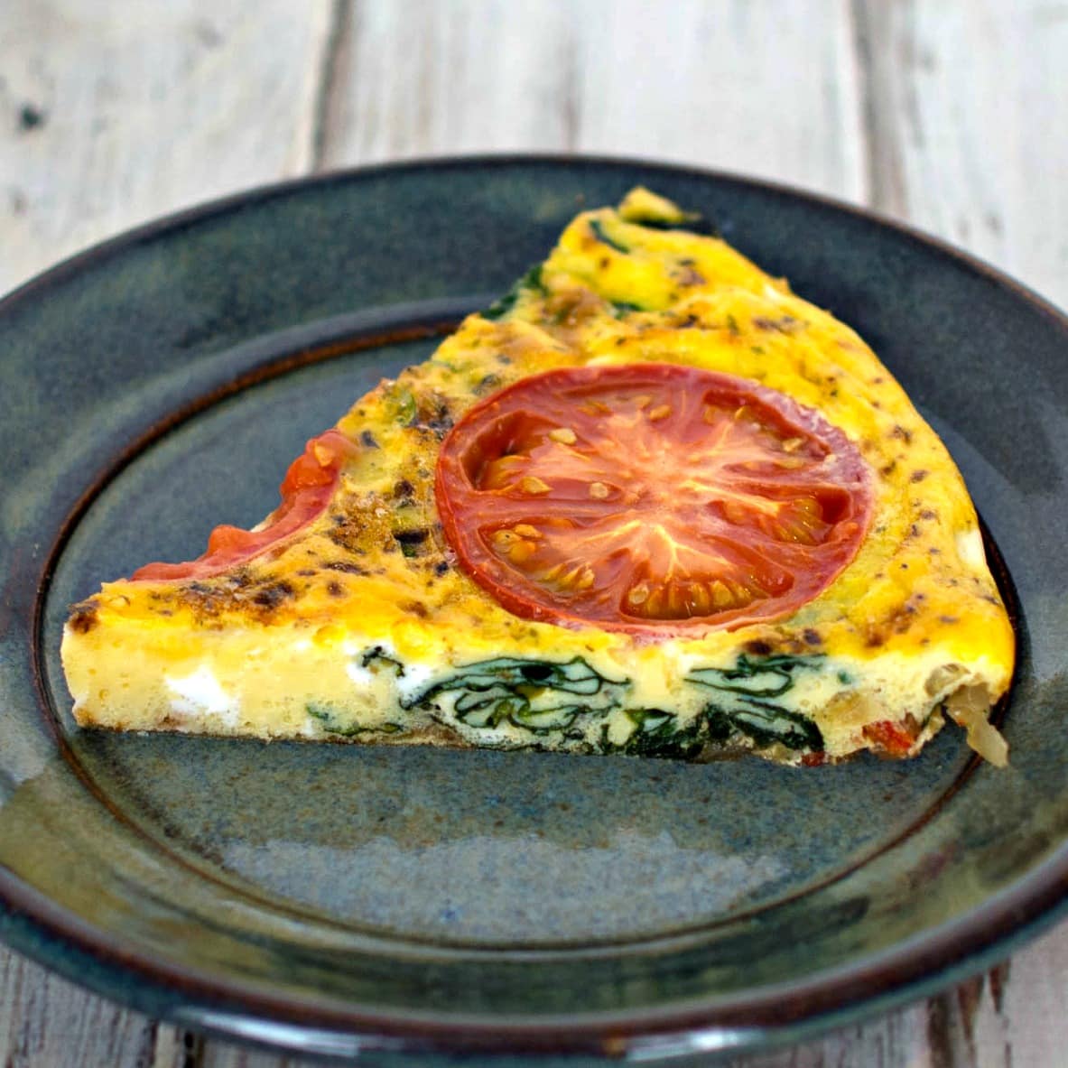 A slice of spinach and tomato quiche on a plate.