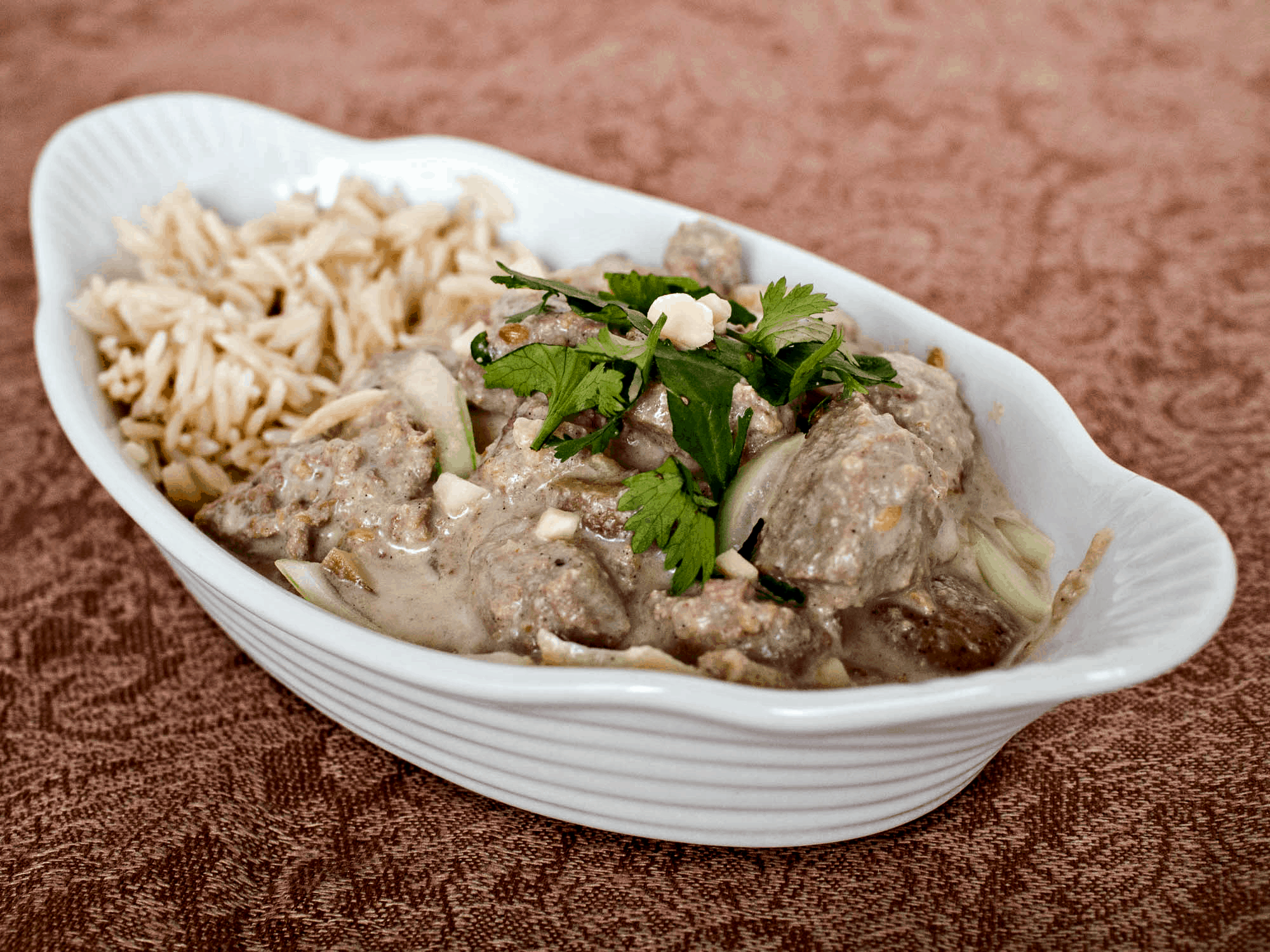A white bowl with meat and rice in it.