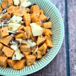 A bowl of sweet potatoes with raisins on a wooden table.