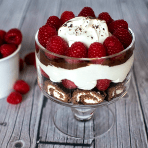 A trifle with whipped cream and raspberries in a glass.