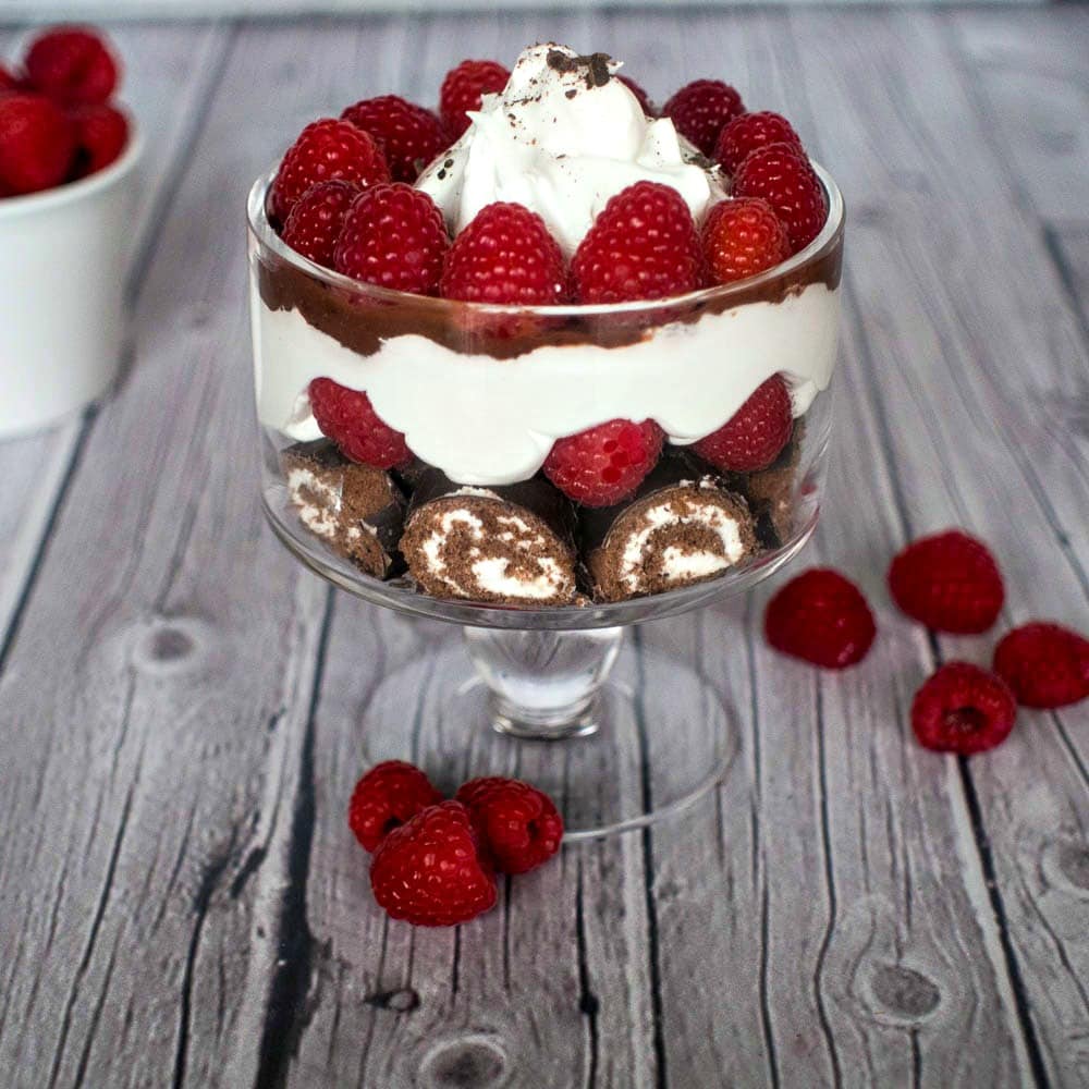 A chocolate raspberry trifle in a glass with whipped cream and raspberries.