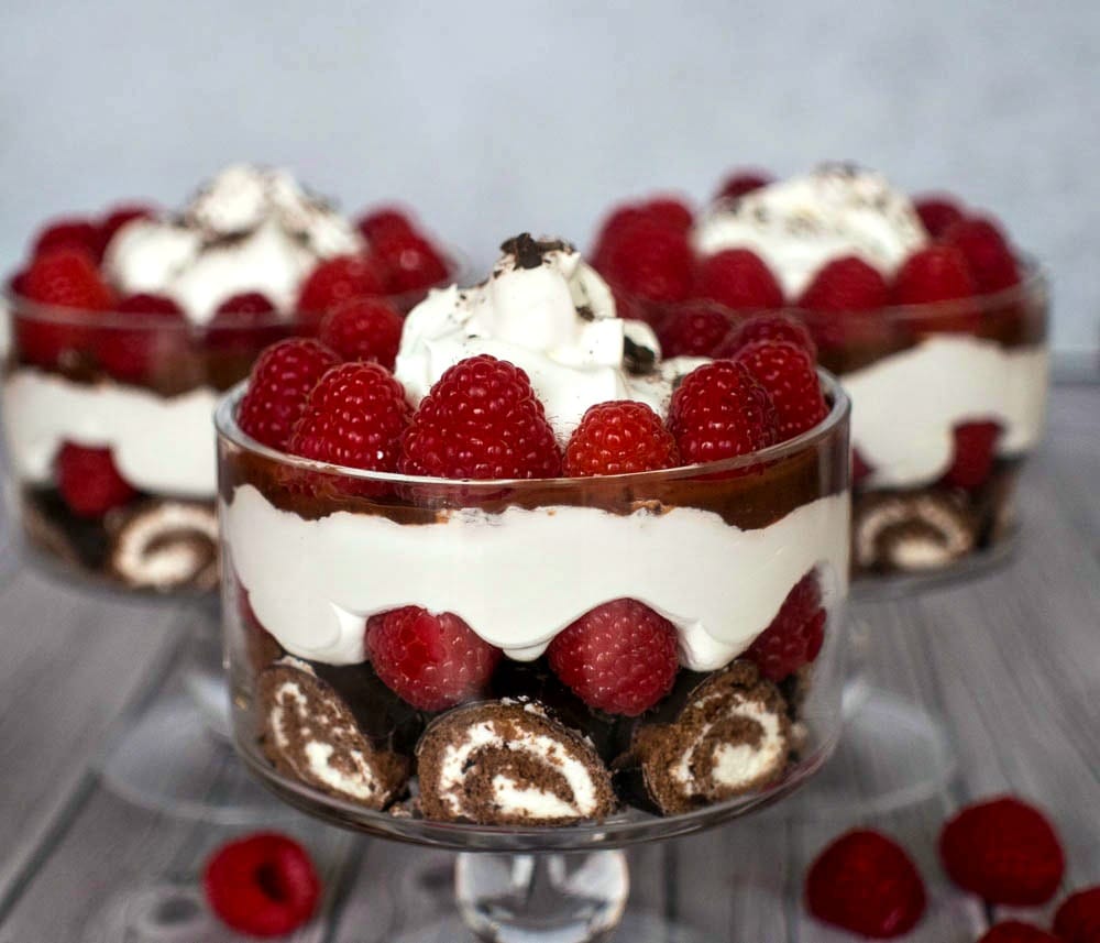 A trio of trifles with whipped cream and raspberries.