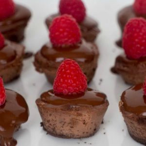 Chocolate raspberry tarts with chocolate ganache and raspberries on a white plate.