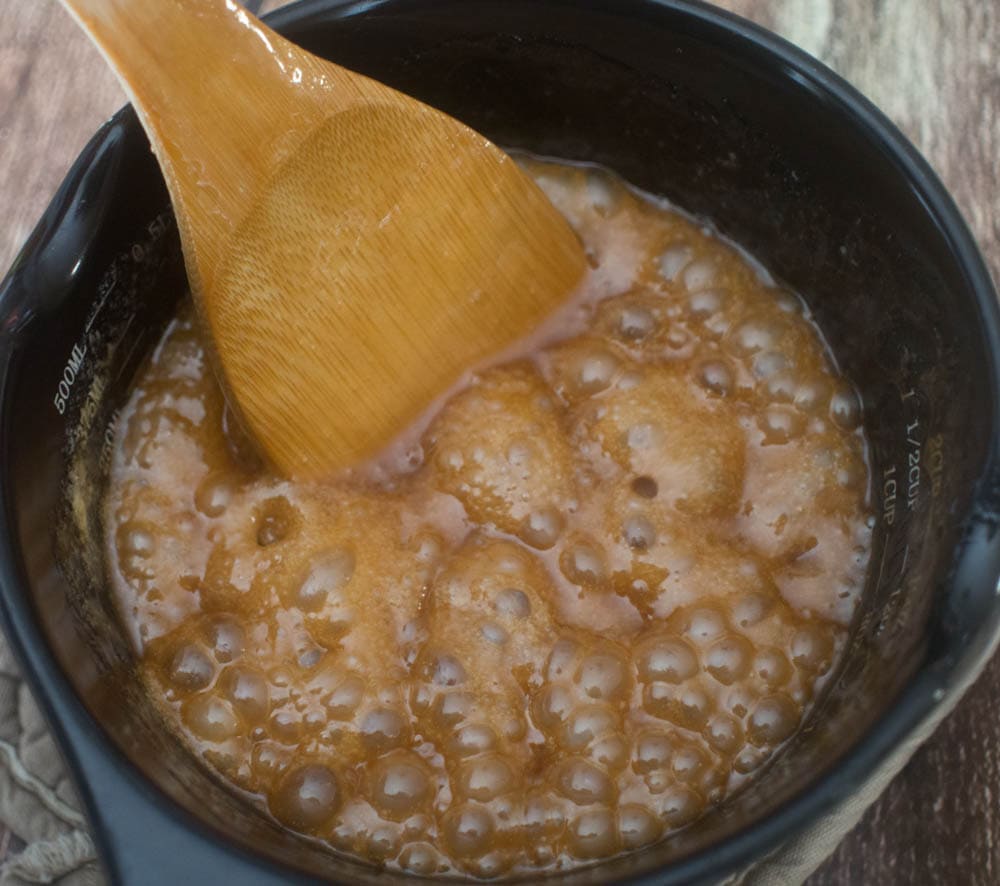 A wooden spoon is being used to stir a brown sauce.