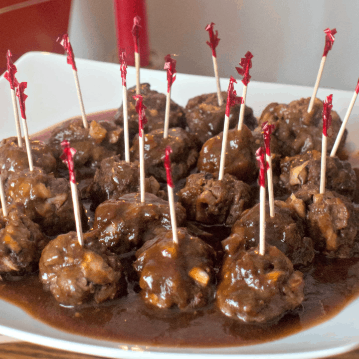 Meatballs with gravy and toothpicks on a plate.