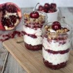 Two jars of cherry and pomegranate parfaits on a cutting board.