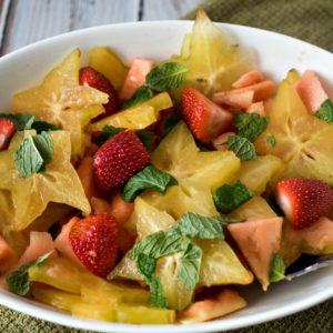 A bowl of fruit salad with strawberries and mint.
