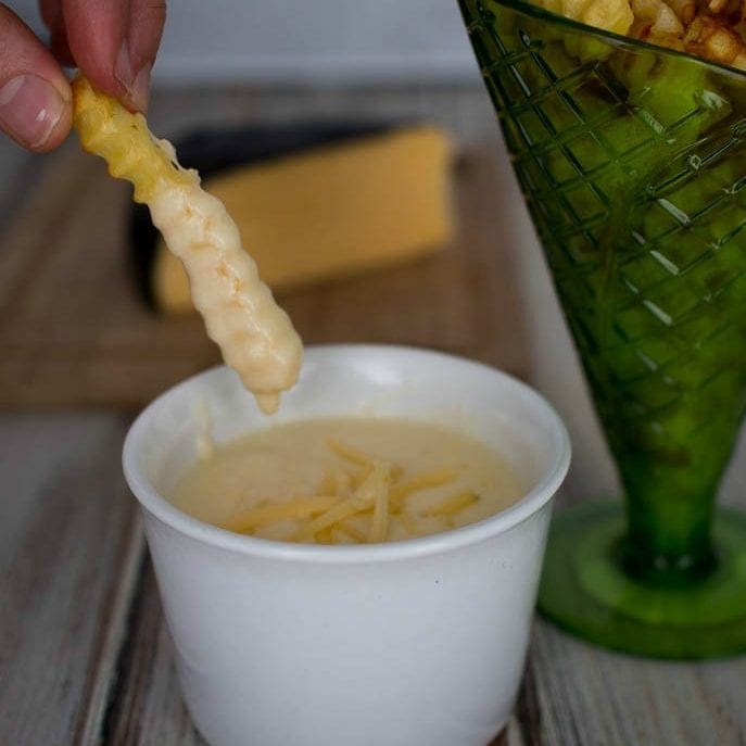 Gouda Cheese Sauce in a bowl with a fry being dipped into it.