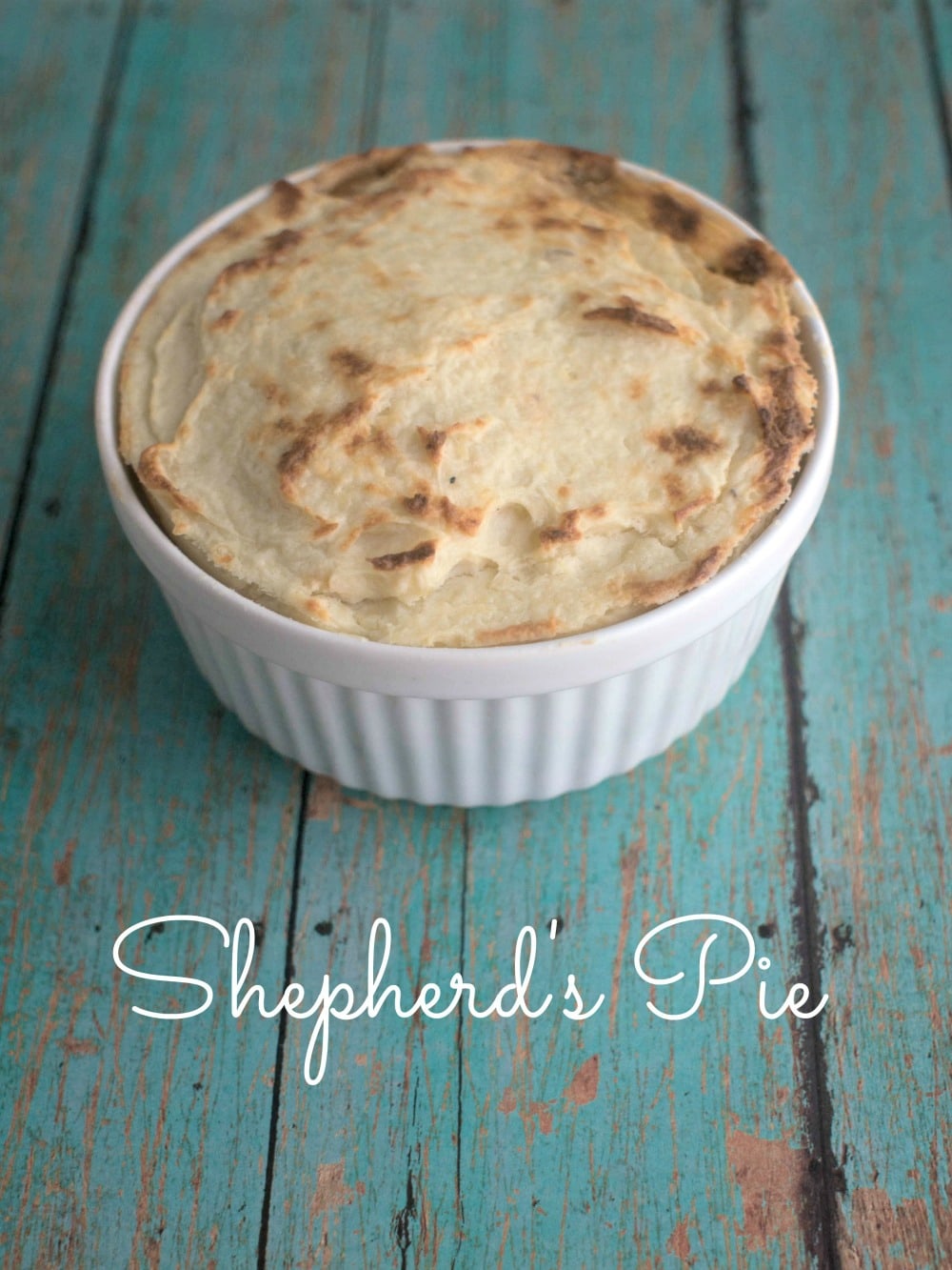 Shepherd's pie in a white bowl on a wooden table.