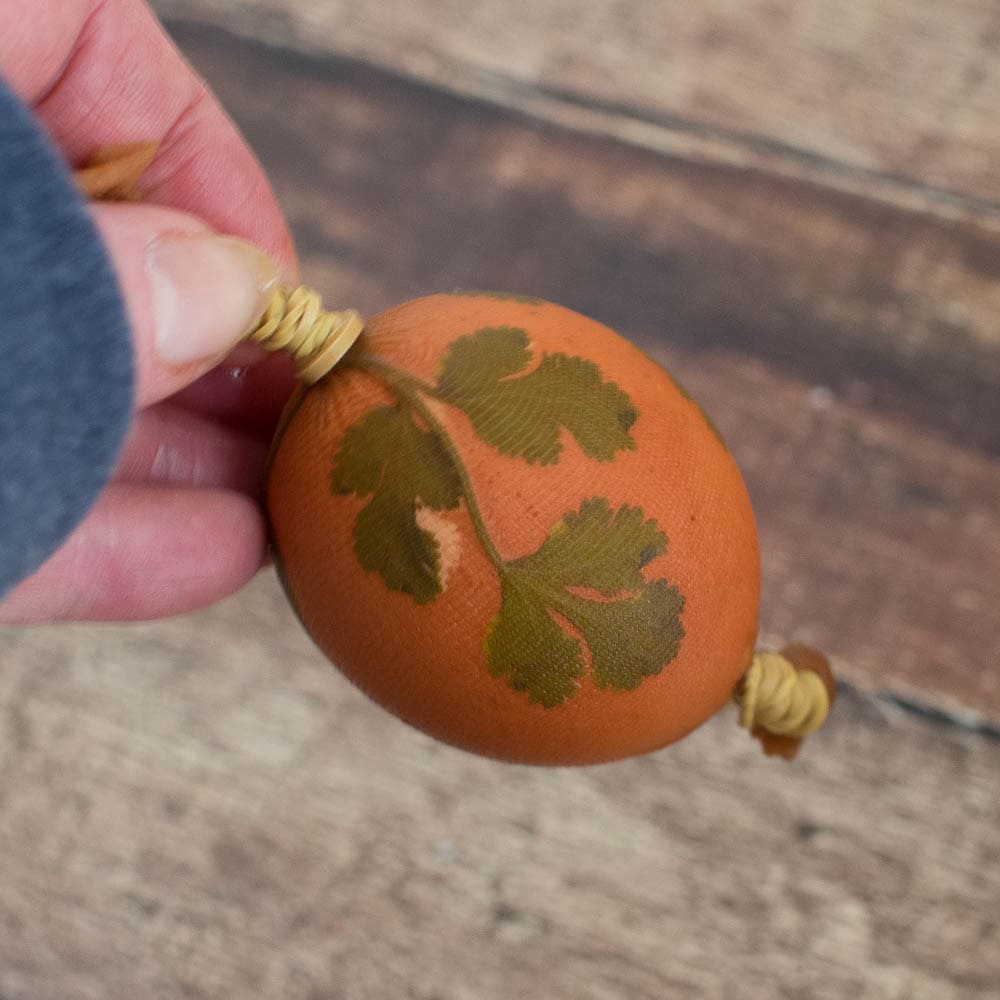 A hand decorated with an herb stenciled design holding an Easter egg.