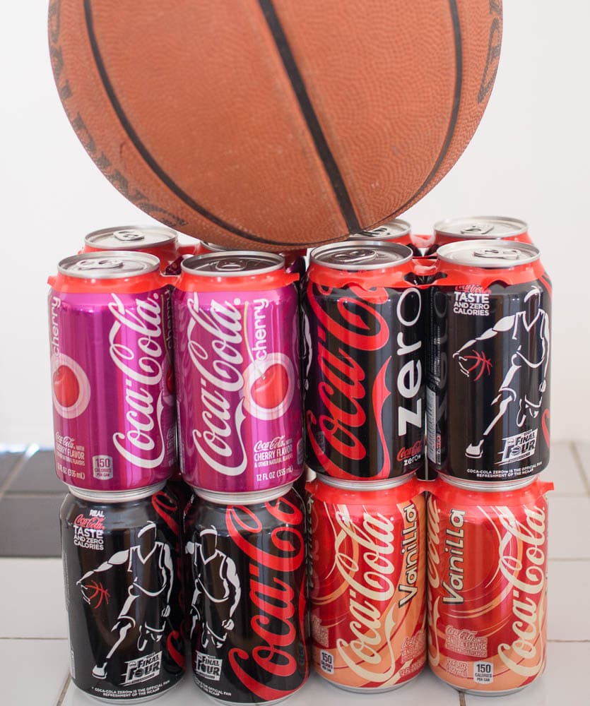 A bunch of cans of Coke Zero sitting next to a basketball.