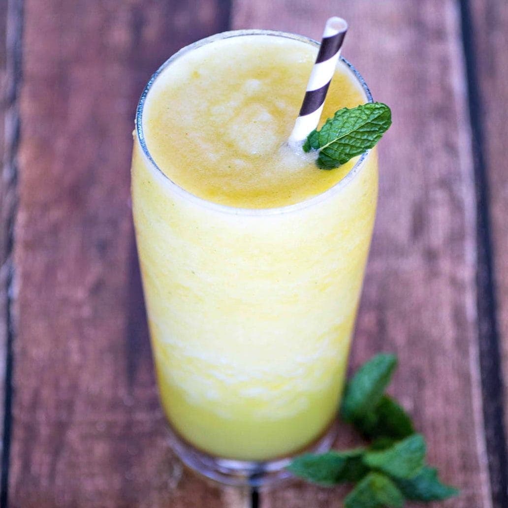 Closeup of pineapple smoothie with sprig of mint and a pineapple.