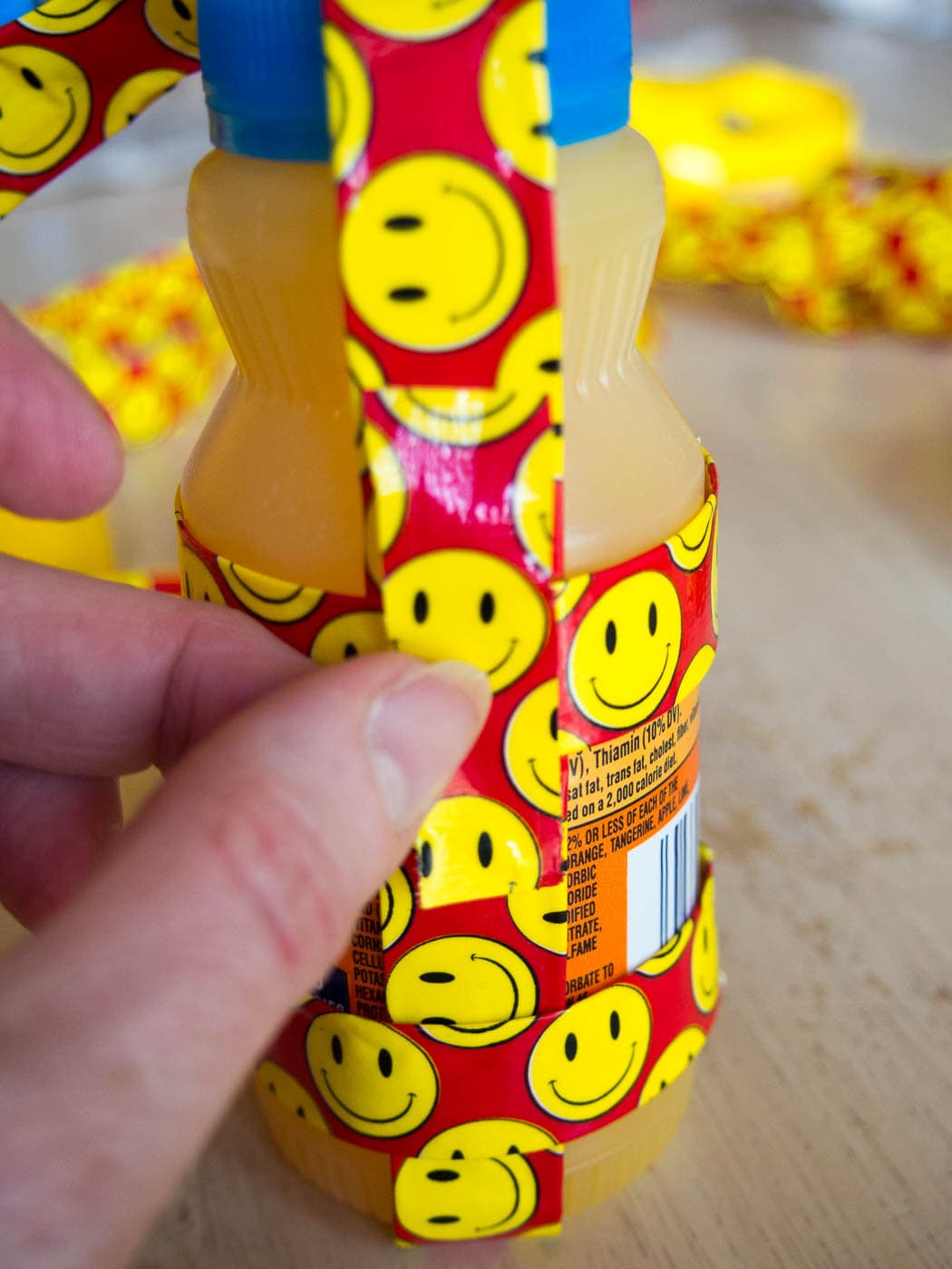 A person is wrapping a smiley face on a bottle of juice using duct tape.