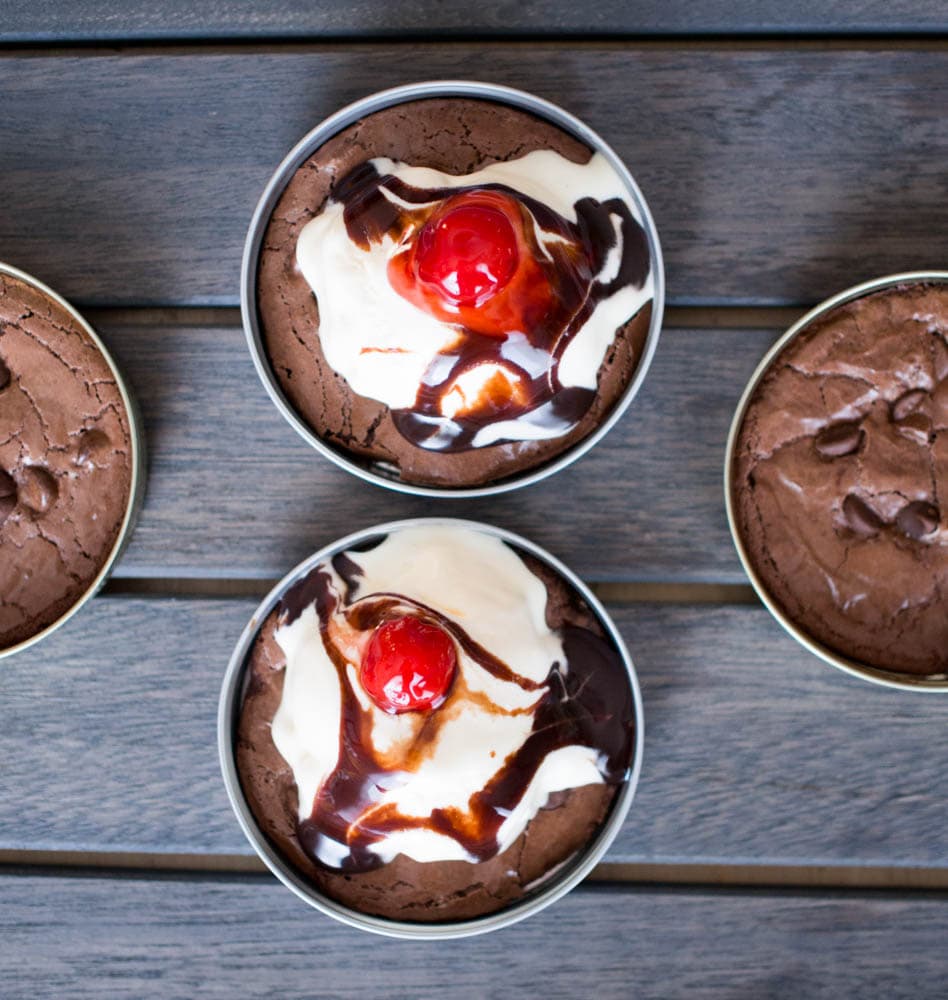 Three chocolate desserts in tins on a wooden table, including brownie and cookies.