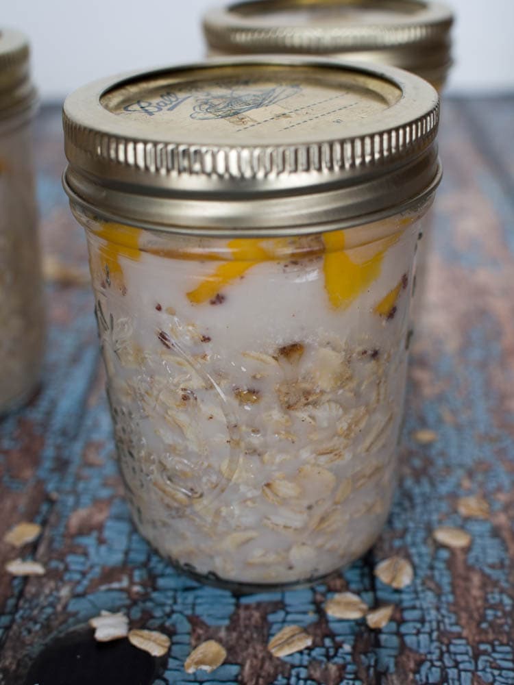 Mango overnight oatmeal in mason jars on a wooden table.