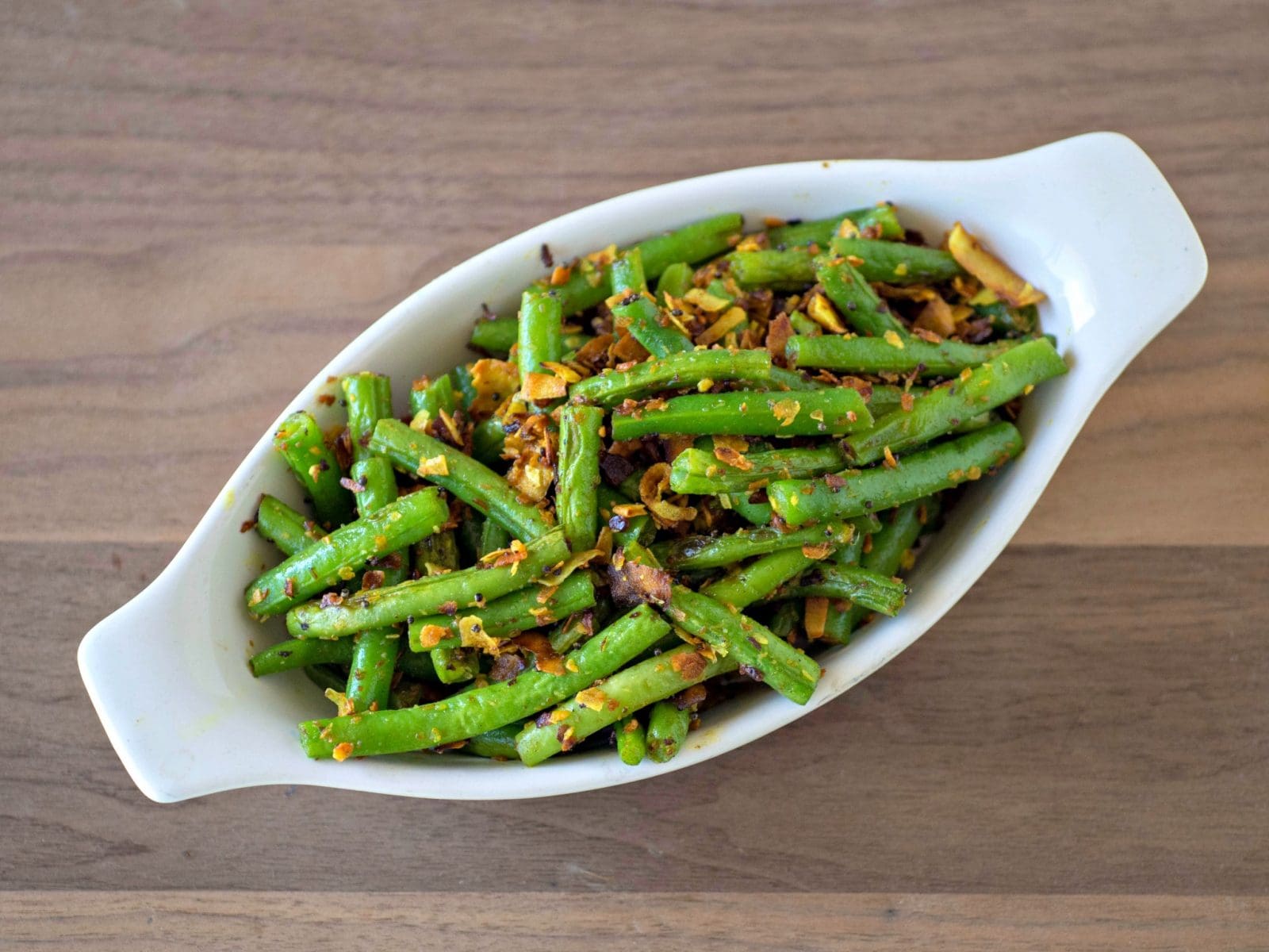 Green beans sauteed in a white bowl on a wooden table.