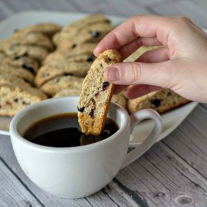 A person is dipping a walnut biscotti into a cup of coffee.