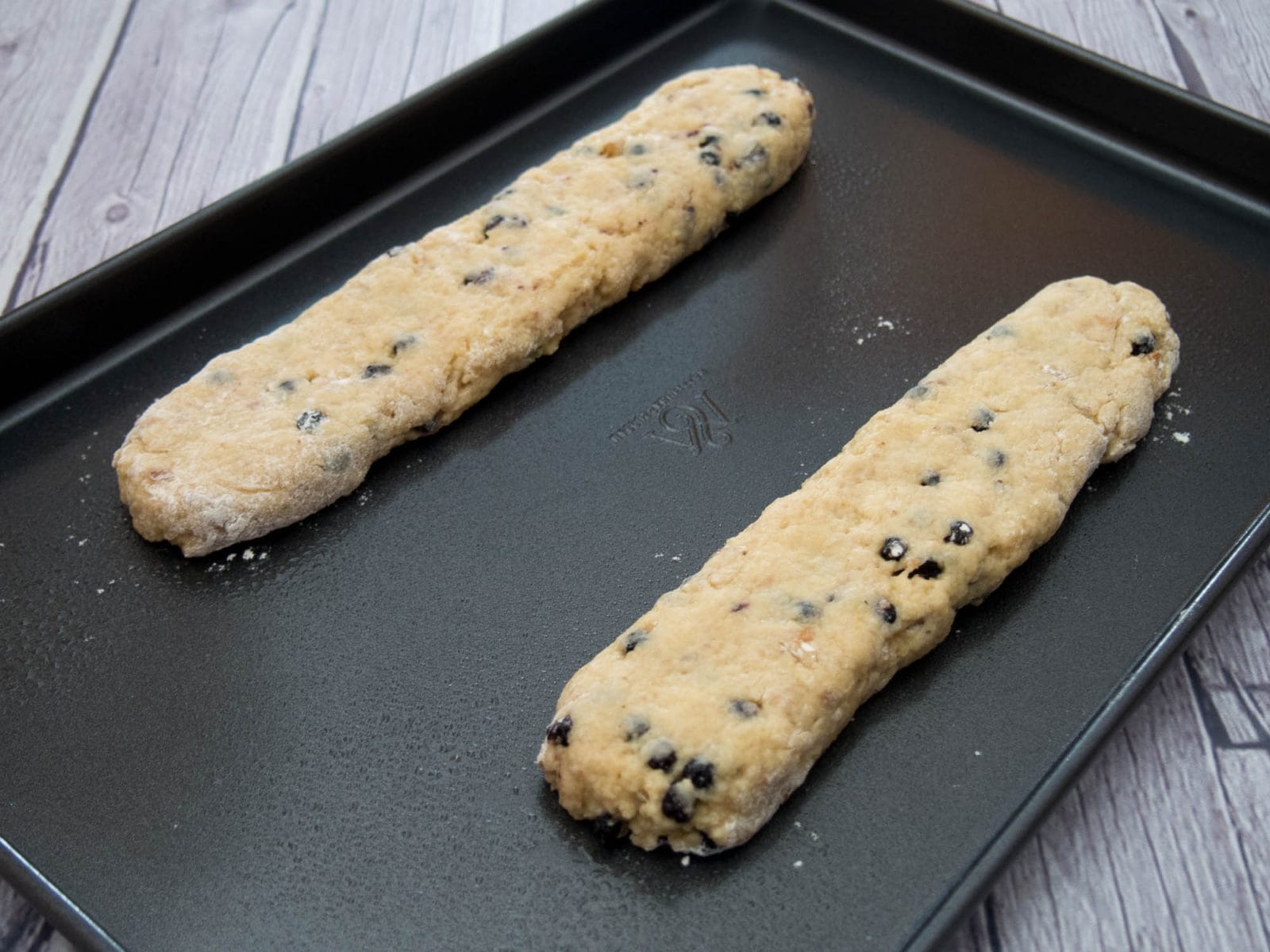 Two walnut biscotti cookies on a baking sheet with chocolate chips on them.