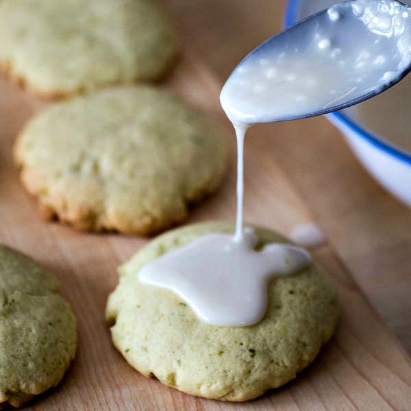 A spoon is drizzling icing onto sugar cookies.