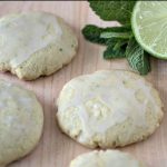 Mojito sugar cookies with icing and mint leaves on a cutting board.