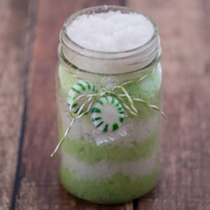 A mason jar filled with green sand and candy canes, featuring a peppermint sugar scrub inside.