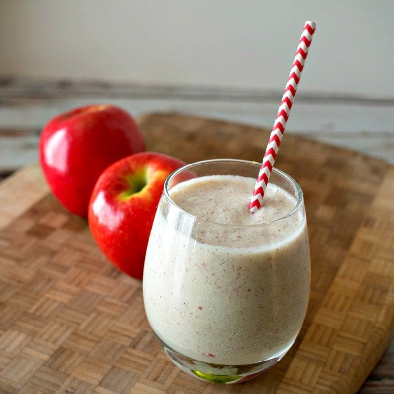 Apple smoothie in a glass with a red polka dot straw on a cutting board.