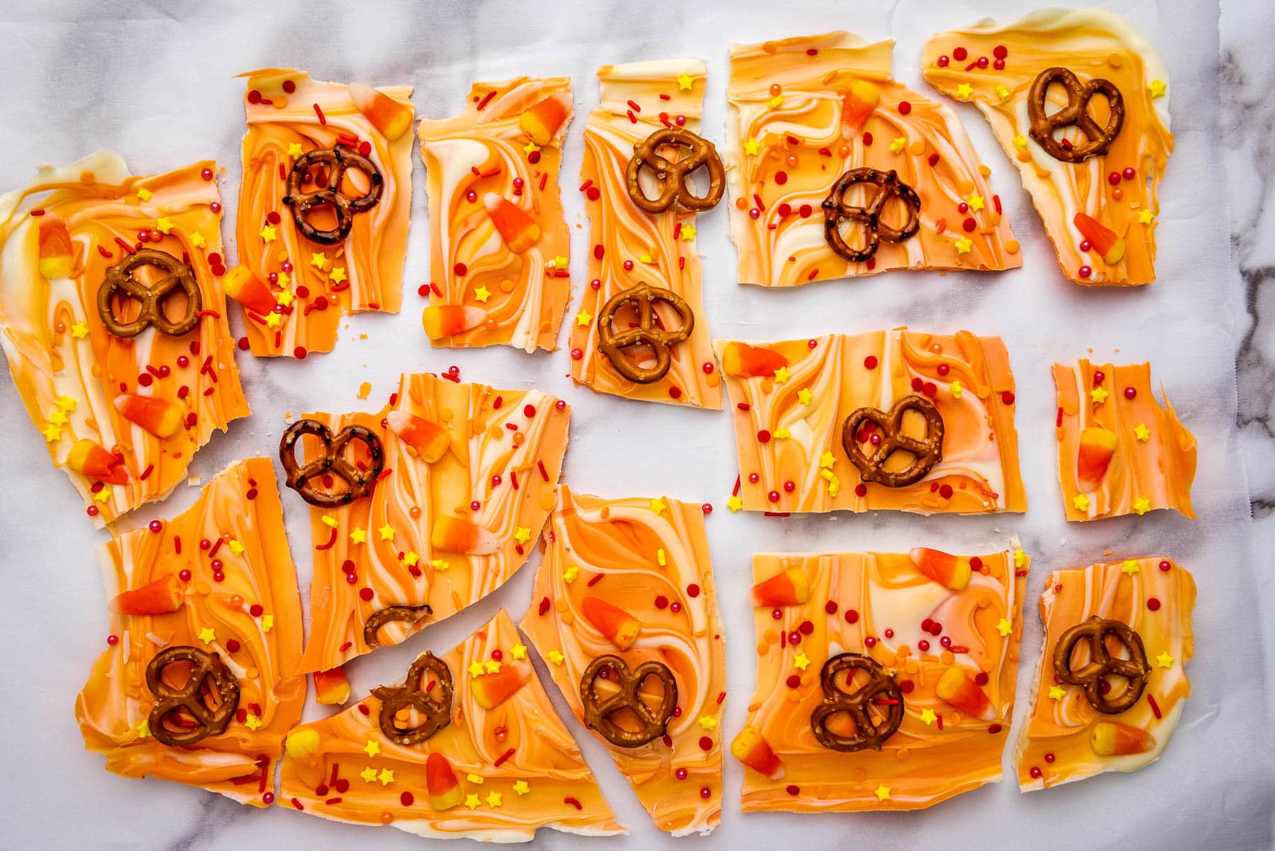 Orange pretzel bark with pretzels on a marble countertop.