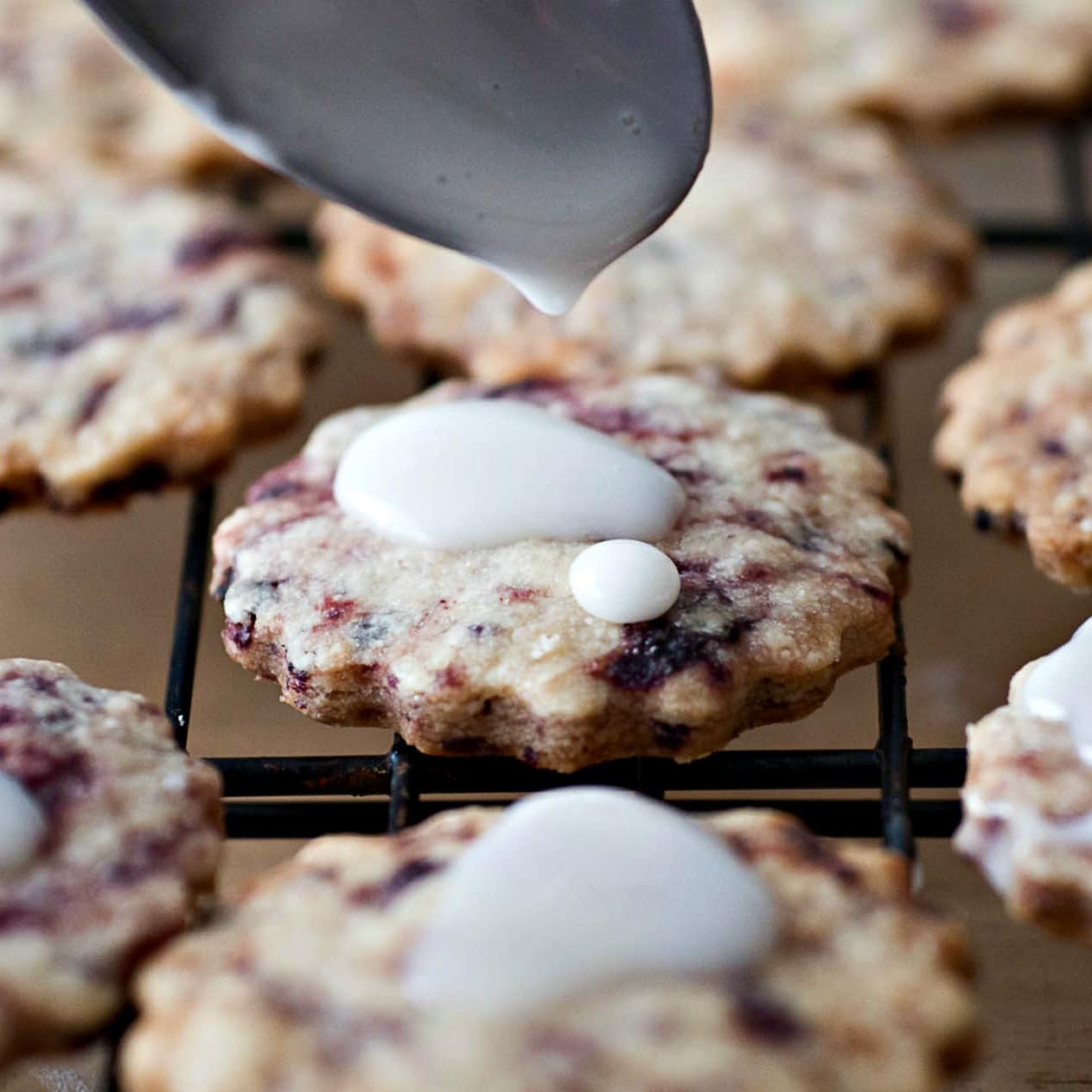 A white icing is being poured onto a rack of cookies.