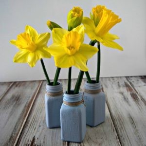 Three blue mason jars filled with yellow daffodils.