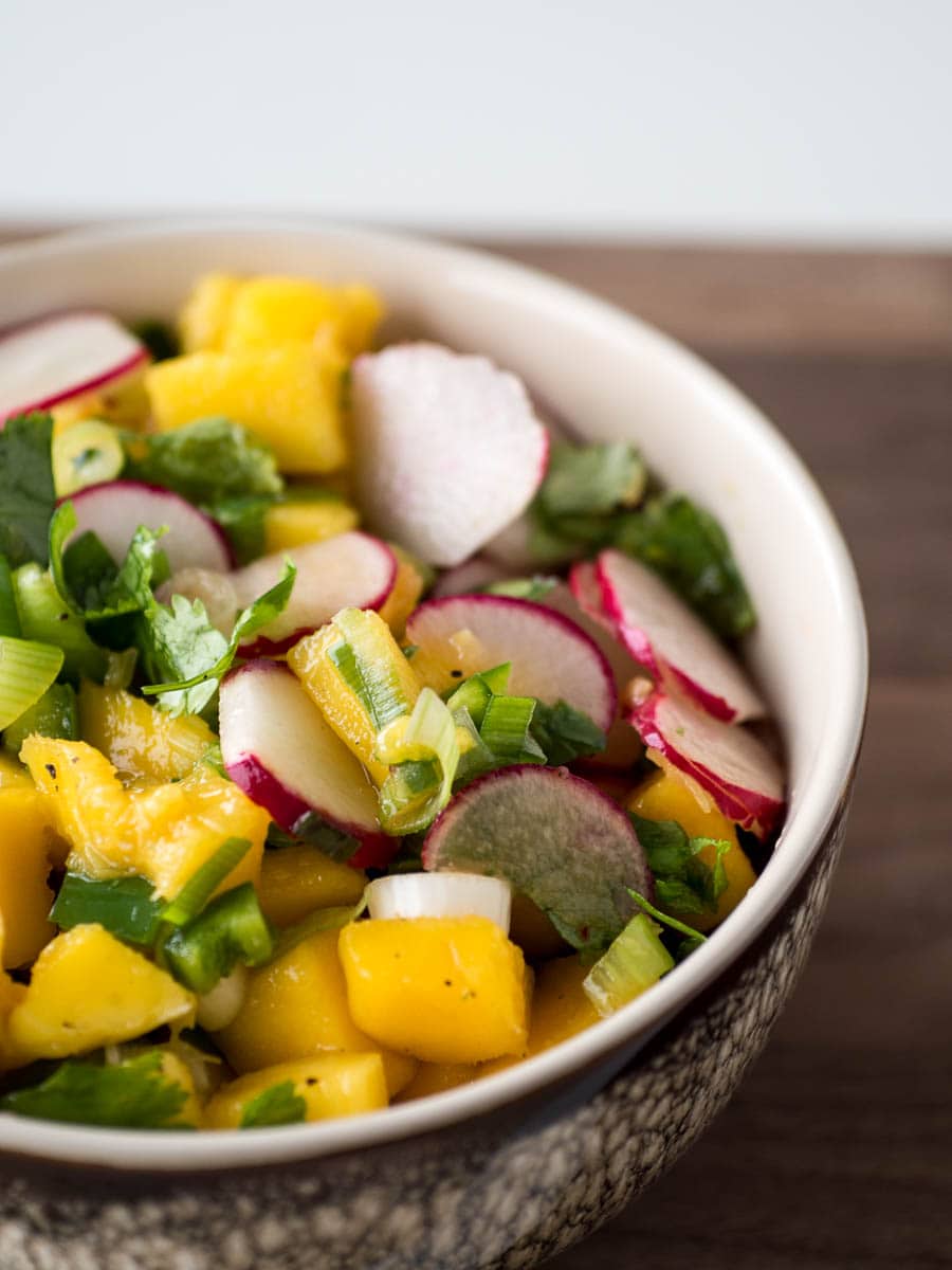 A bowl of mango and radishes in a wooden bowl.
