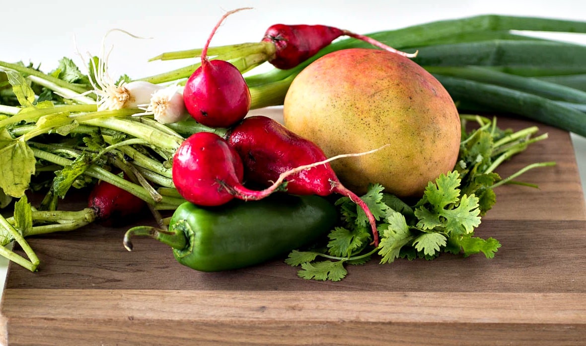 A cutting board with radishes, mangoes and radishes.