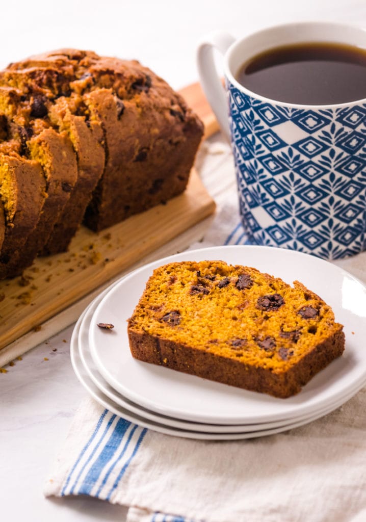 slice of chocolate chip pumpkin bread on a plate with loaf in the background