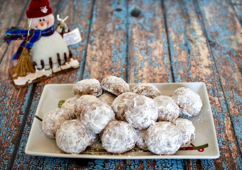 Powdered sugar cookies on a plate with a snowman, also known as Russian tea cakes.
