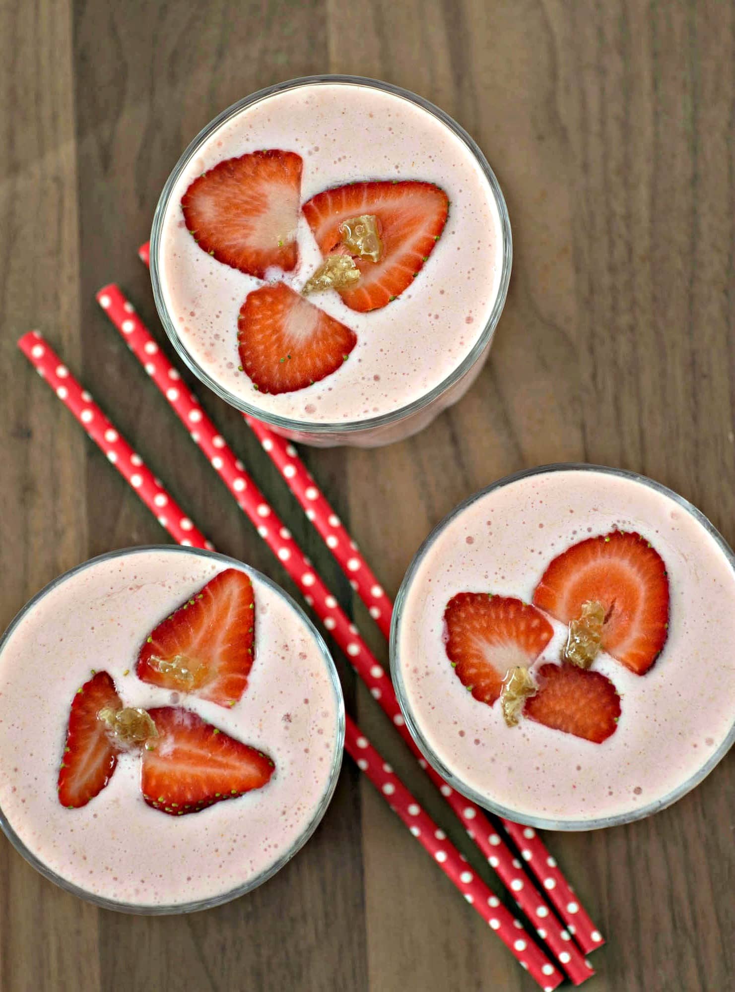 Three glasses with strawberries and straws on top.