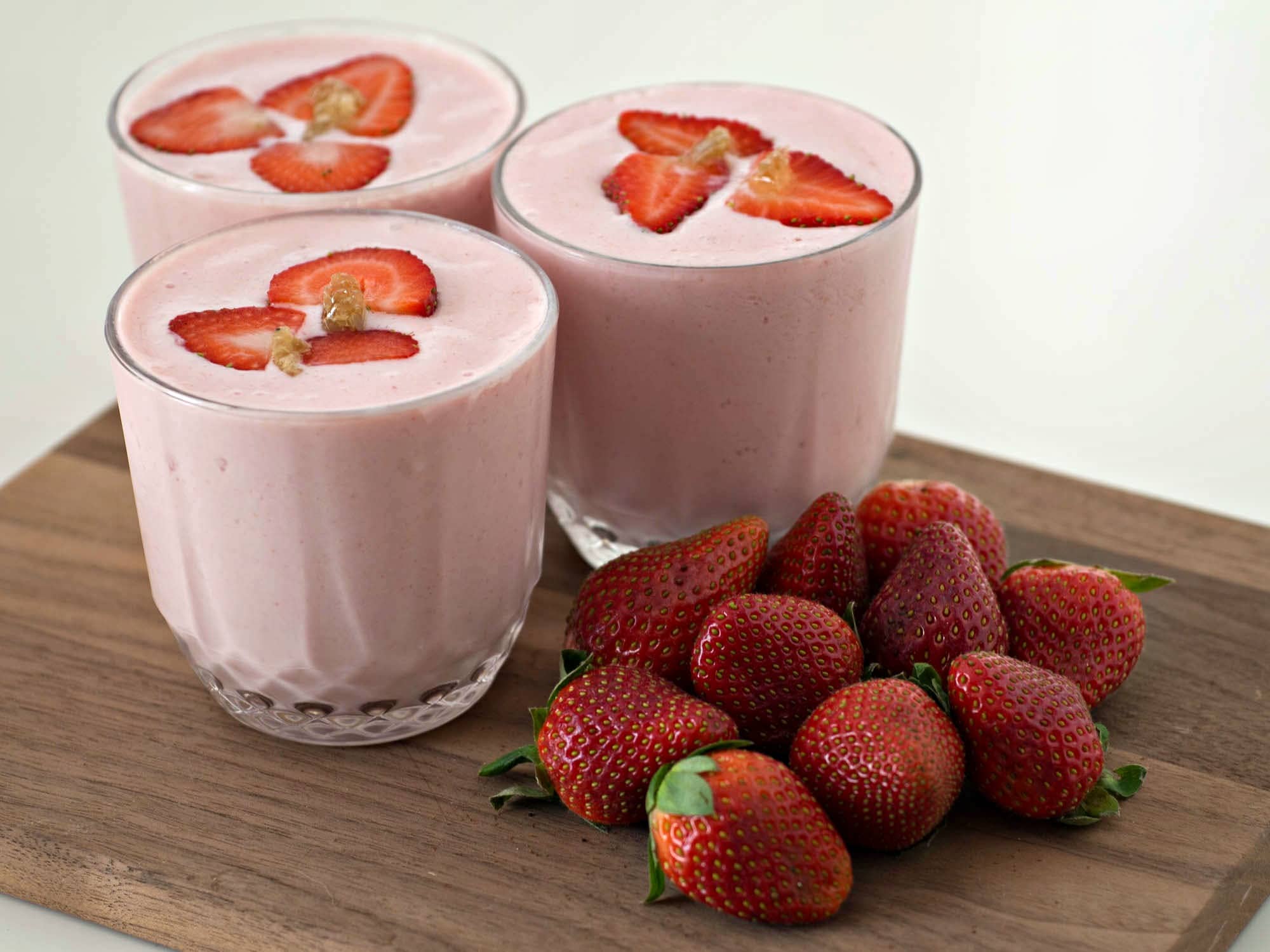 Three glasses of strawberry smoothie on a wooden cutting board.