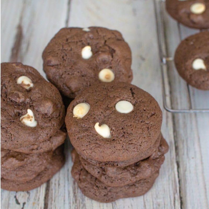 Stack of chocolate cookies with white chocolate chips on a wooden surface.